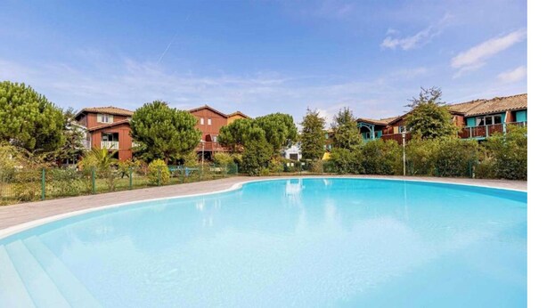 Una piscina con cubierta de madera, rodeada de casas con tejados rojos y árboles verdes.