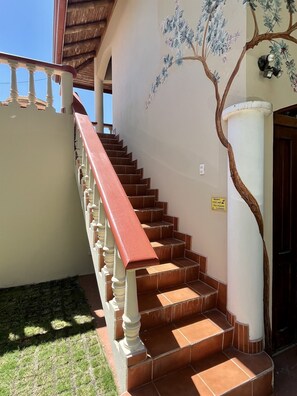 Eine Treppe mit roter Handlauf, weißen Balustraden und einer Wandmalerei eines Baumes.