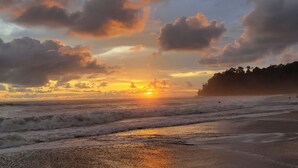 Een strand met golven, een zonsondergang en een bebost gebied.