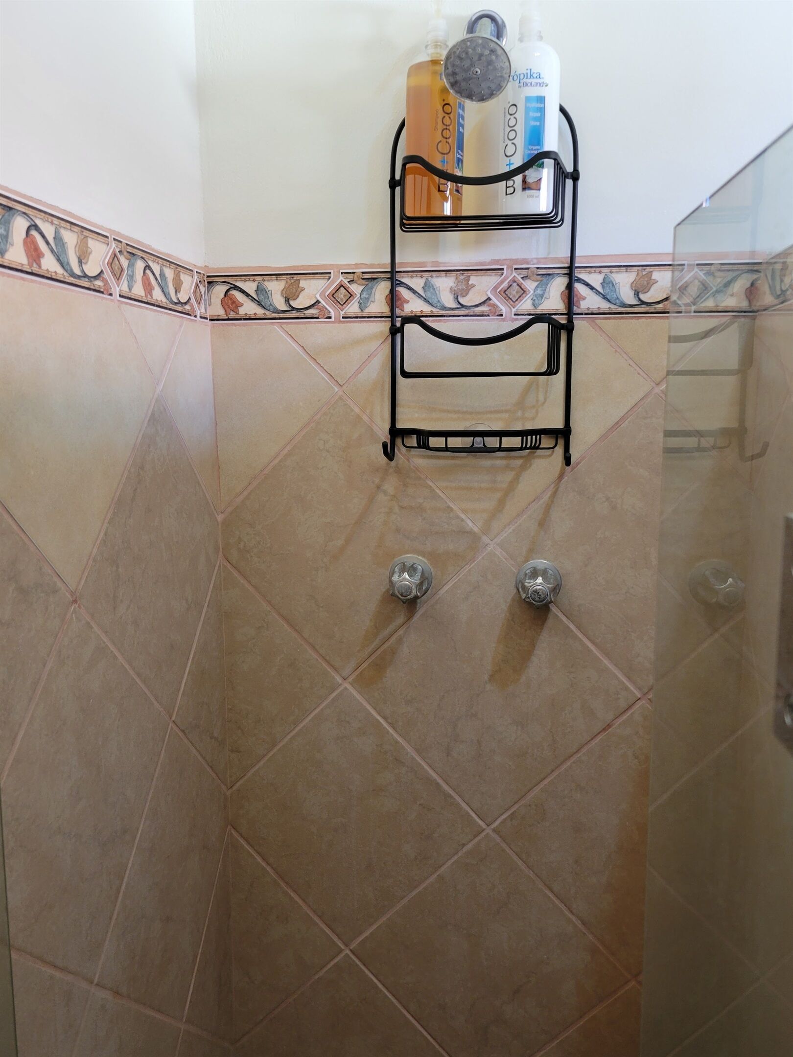 Un baño con ducha, paredes de azulejos y un estante metálico con artículos de aseo.