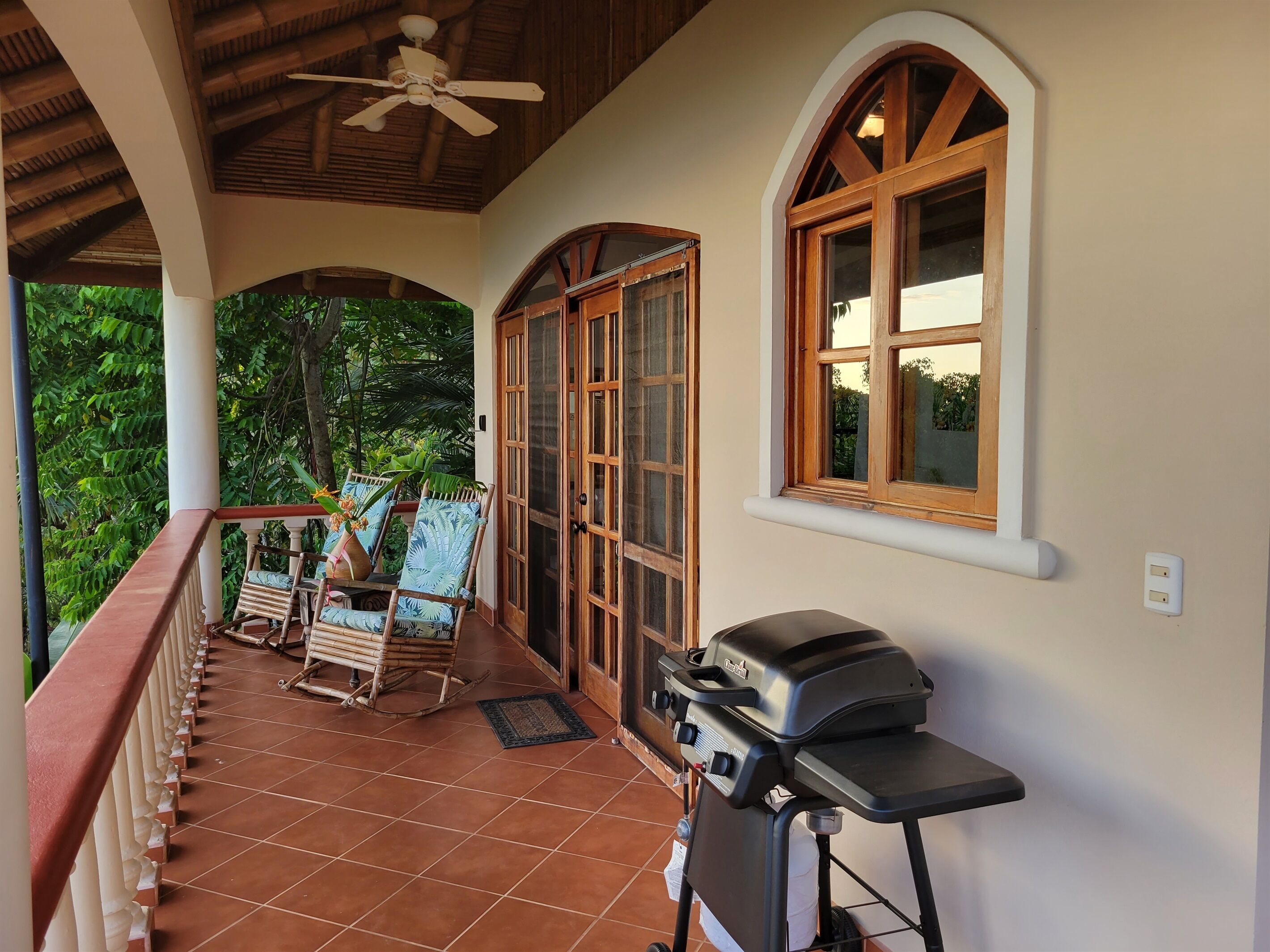 A covered porch with a grill, rocking chairs, and a view of greenery.