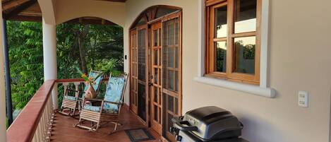 A covered porch with a grill, rocking chairs, and a view of greenery.