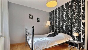 A bedroom with a bed, bedside lamps, a radiator, and a patterned wallpaper. - The Monthorin Valley (La Bazouge-du-Désert)