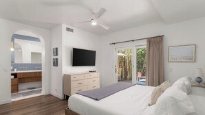Une chambre avec un lit, une télévision, un ventilateur de plafond, une salle de bain avec un meuble-lavabo et une vue sur l’extérieur.