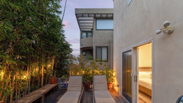Un balcon avec deux fauteuils de relaxation, une terrasse en bois et un bâtiment au design moderne, doté d’une porte vitrée donnant accès à une chambre.