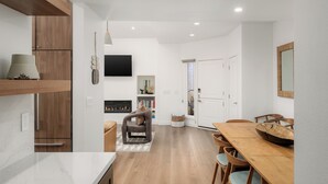 Une cuisine moderne avec des meubles en bois, un coin repas comprenant une table et des chaises en bois, et un téléviseur à écran plat fixé au mur.