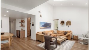 Un salon moderne avec un plancher en bois, un canapé marron, une table à manger et un coin cuisine doté de meubles en bois.