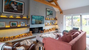 A living room with a fireplace, a television, and a large window. - Some homes are made for holidays,  Surfers Roost is made for time well spent together. (Croyde)
