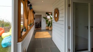 A hallway with a wooden bench, a sunburst mirror, and a door leading to a room. - Some homes are made for holidays,  Surfers Roost is made for time well spent together. (Croyde)