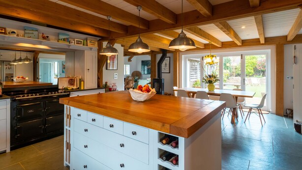 A kitchen with wooden beams, pendant lights, a central island with drawers, and a dining area with a table and chairs. - Some homes are made for holidays,  Surfers Roost is made for time well spent together. (Croyde)