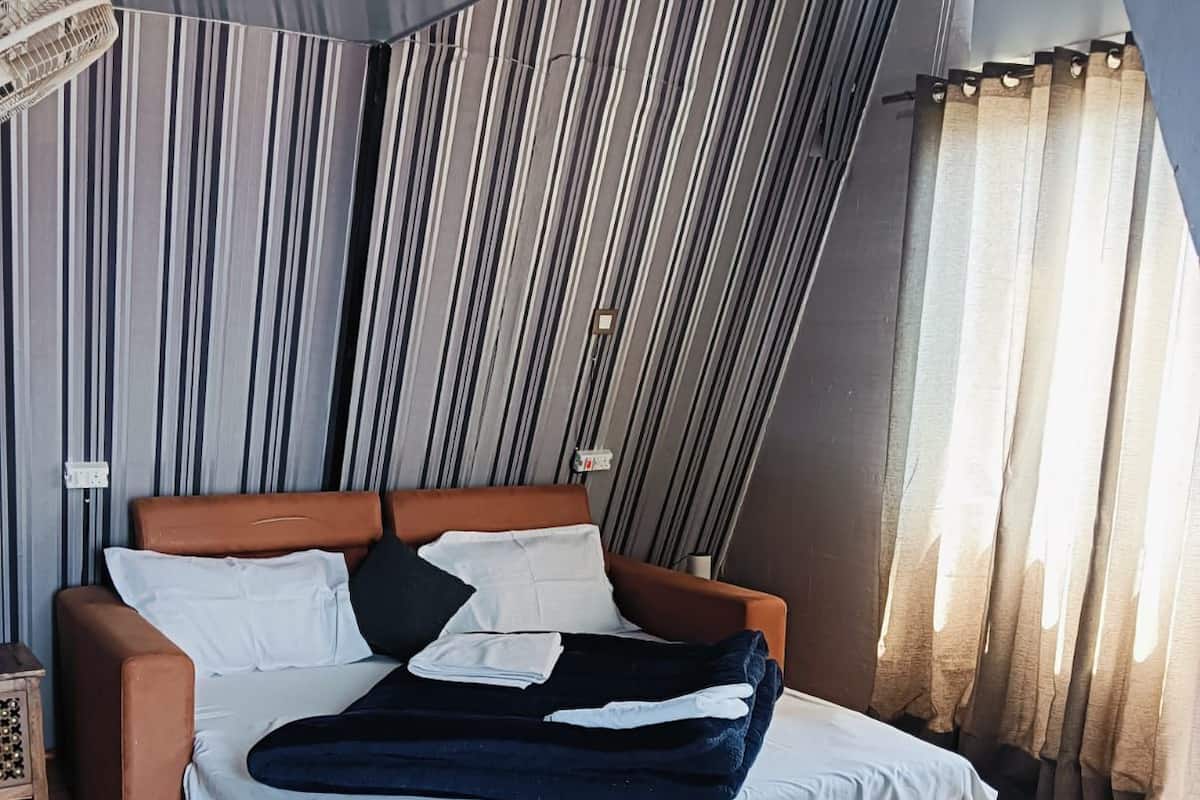 Un dormitorio con cama, ventilador, alfombra y pared a rayas.