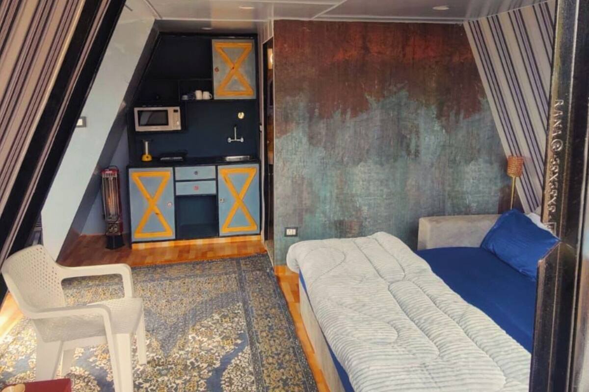 Una habitación funcional con cama, un pequeño escritorio y kitchenette.