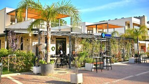 Un restaurant avec une terrasse, des palmiers et un ciel d’un bleu éclatant.