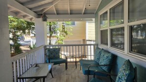 A covered porch with a table and two chairs, a ceiling fan, and a view of the street. - Seafoam Cottage - Beauty in the Heart of Cedar Key (Cedar Key)