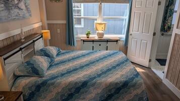 A bedroom with a bed, bedside tables, a window, a door, and a wall decoration.