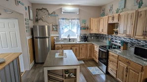 A modern kitchen with wooden cabinets, a stainless steel refrigerator, a built-in oven, and a granite countertop. - Seafoam Cottage - Beauty in the Heart of Cedar Key (Cedar Key)