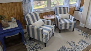 A room with two striped armchairs, a small table, a blue chair, and a window with curtains. - Seafoam Cottage - Beauty in the Heart of Cedar Key (Cedar Key)
