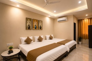 Habitación de hotel con dos camas, una mesita con una planta, un equipo de aire acondicionado y un ventilador de techo.