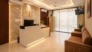 A hotel reception area with a marble wall, a reception desk, a television, a ceiling fan, and a sofa. - Travinities Hotel - The Royal Palace (Indore)