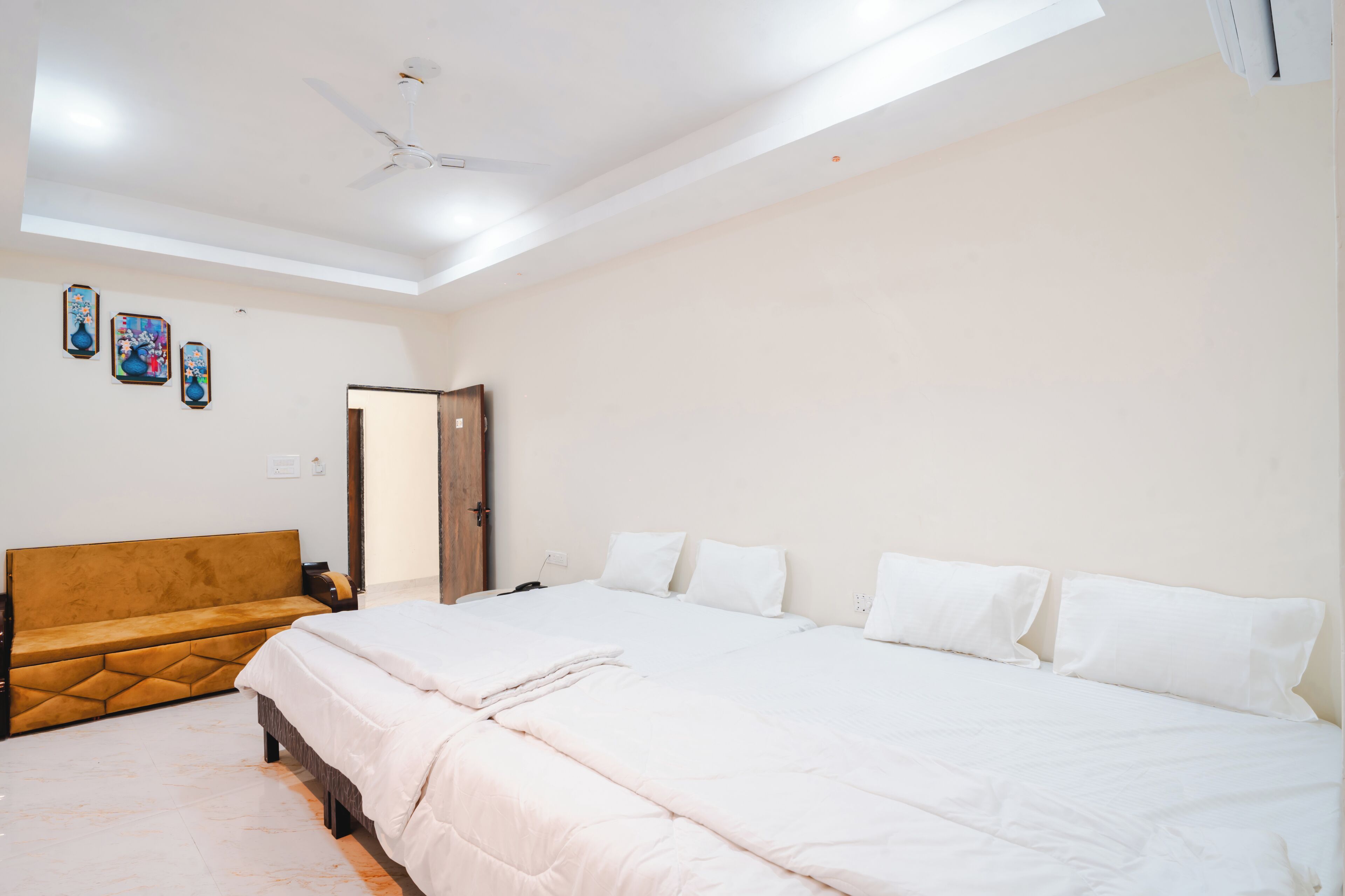 Une chambre à coucher comprenant un lit, un canapé, un ventilateur de plafond et des œuvres d’art accrochées au mur.