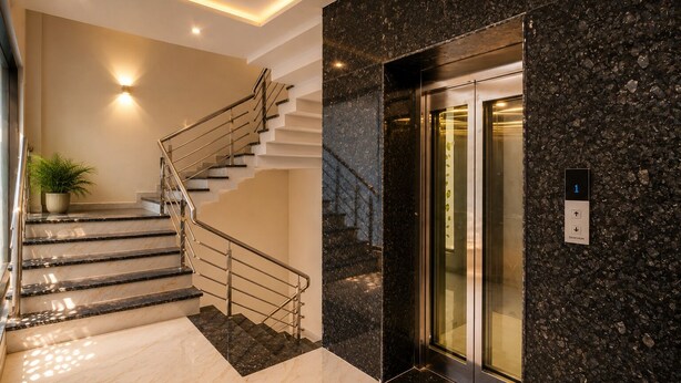 A modern interior with a marble staircase, a potted plant, and an elevator. - Travinities Hotel - The Royal Palace (Indore)