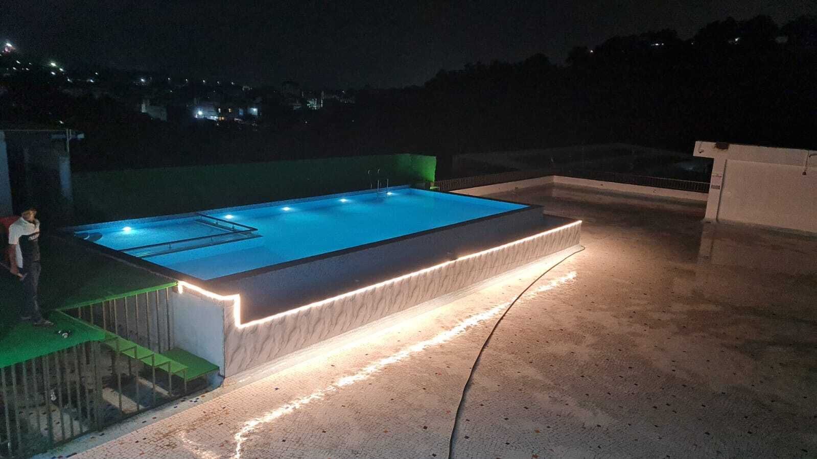 Una piscina rectangular con borde iluminado, rodeada por una solera de hormigón.