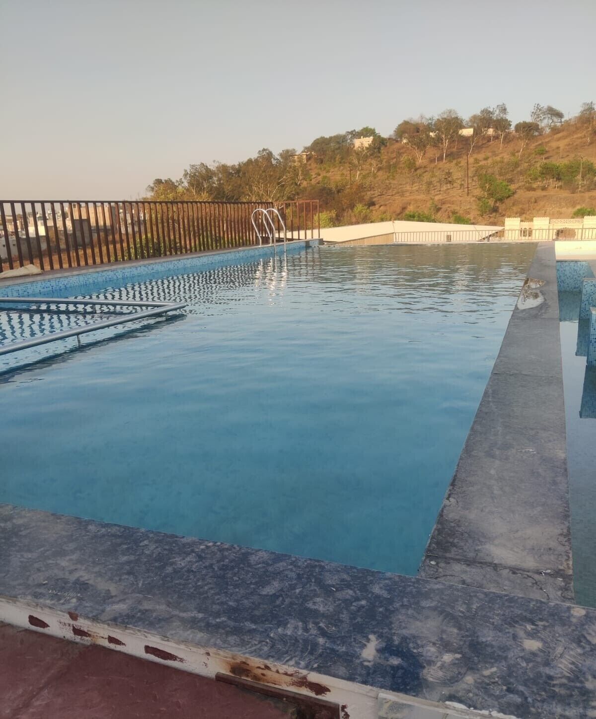 A swimming pool with clear water, a metal ladder, and a wooden fence.