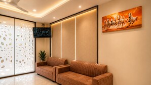A reception area with a sofa, a TV, a plant, and a painting. - Travinities Hotel - The Royal Palace (Indore)