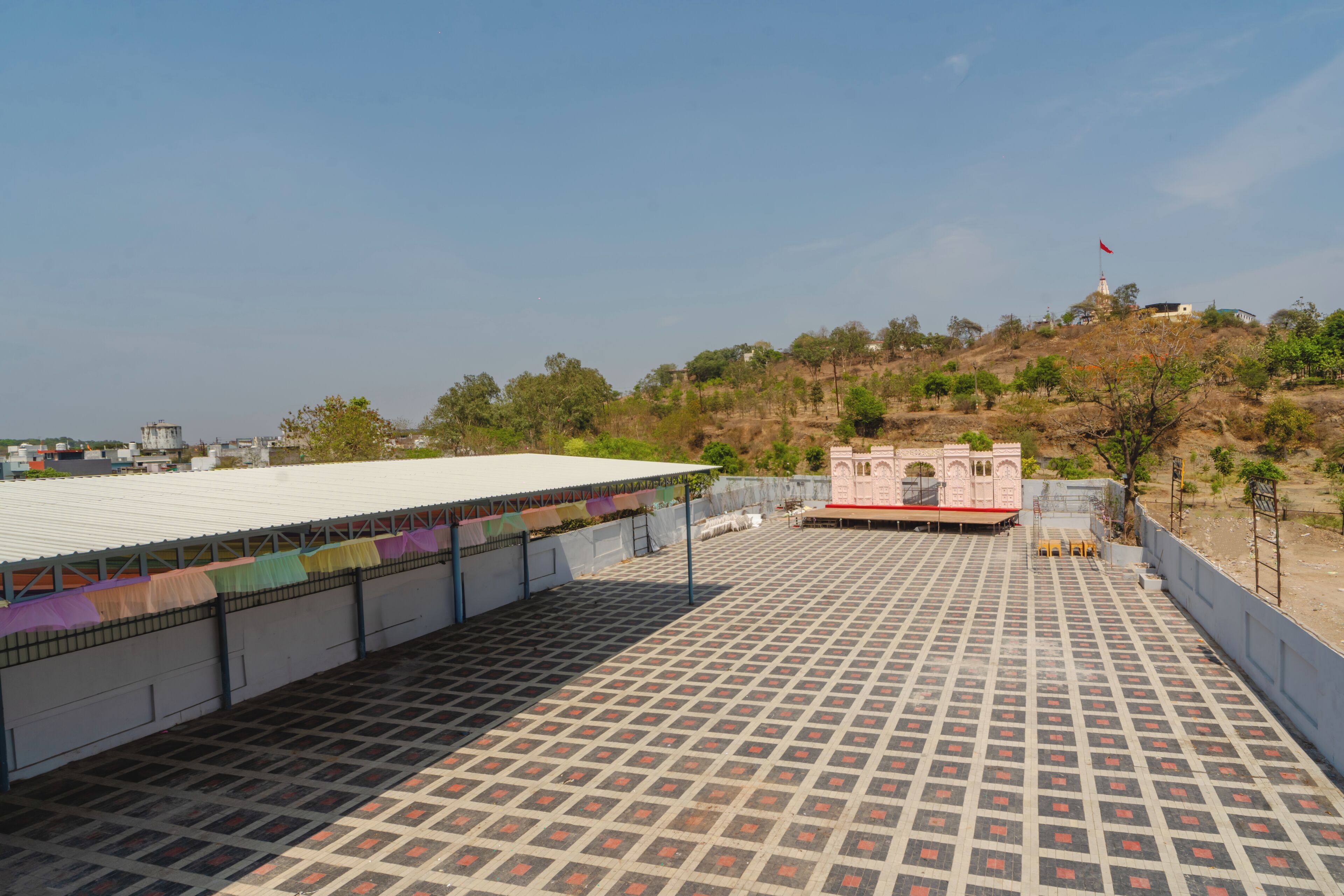 Una terraza en la azotea con suelo estampado, una estructura rosa pequeña y vistas a una colina con vegetación escasa.