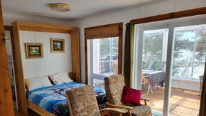 A room with a bed, two patterned chairs, a table, and a view through large windows. - Superb cottage with view and privileged access to Preissac Lake - Pets allowed (Preissac)