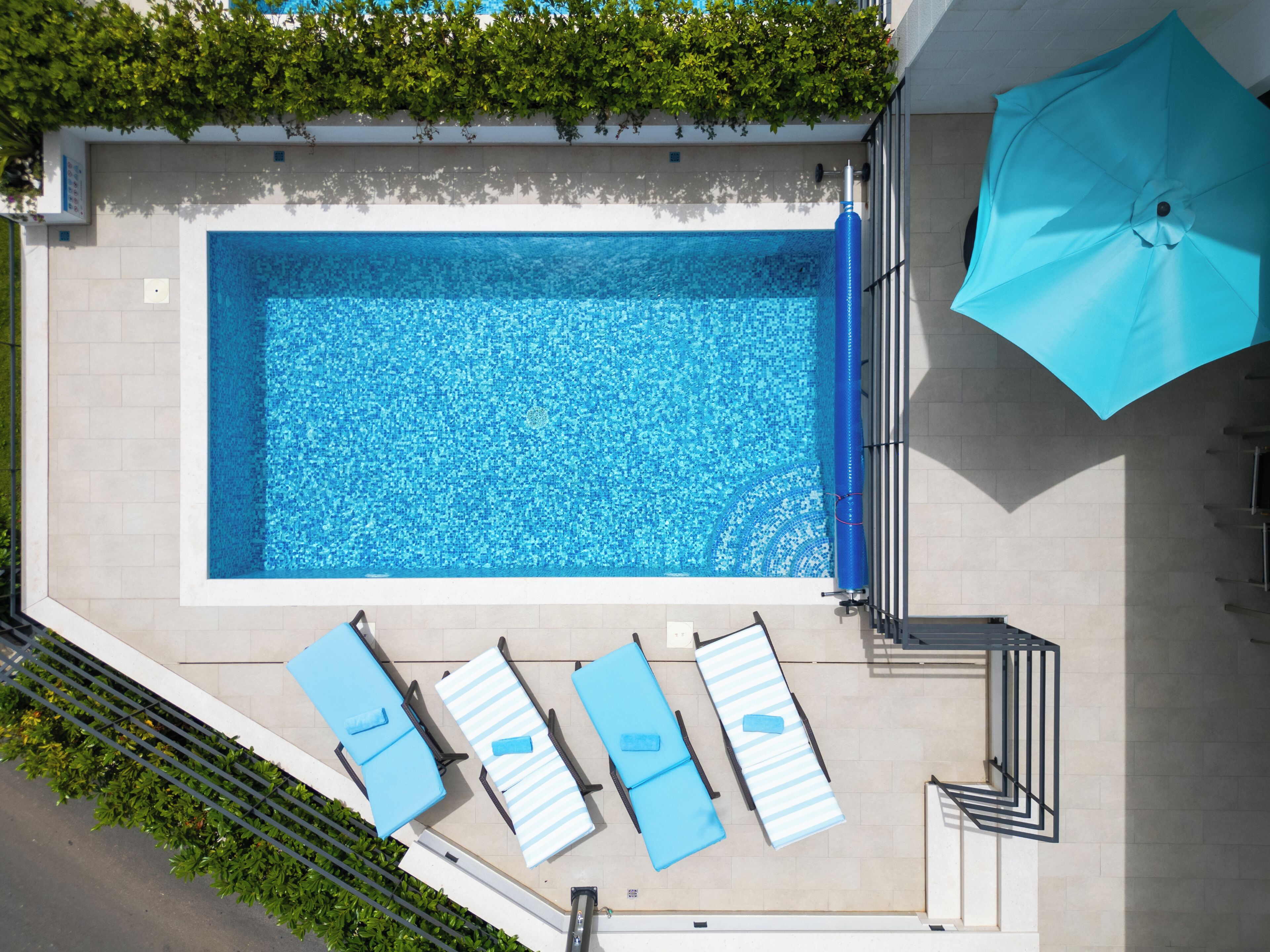 Una piscina en la azotea con revestimiento de mosaicos azules, rodeada de sillones de descanso y una sombrilla grande.