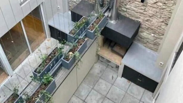 Un espacio exterior moderno con un muro de ladrillo, estructuras metálicas y una jardinera con plantas.