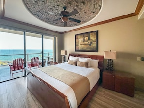 A hotel room with a large bed, a ceiling fan, a painting, and a view of the ocean. - The Iconic Beachfront 3BR Condo (Puerto Peñasco)