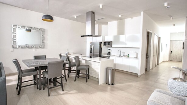 A modern kitchen with a central island, a dining area with a table and chairs, and a large mirror on the wall. - Beachfront 1BR High-floor Panoramic Views (Puerto Peñasco)