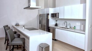 A modern kitchen with white cabinetry, stainless steel appliances, a central island, and bar stools. - Beachfront 1BR High-floor Panoramic Views (Puerto Peñasco)