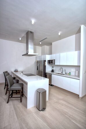 A modern kitchen with white cabinetry, stainless steel appliances, a central island, and bar stools. - Beachfront 1BR High-floor Panoramic Views (Puerto Peñasco)