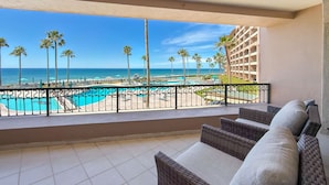 Ein Balkon mit Korbmöbeln, ein Schwimmbad, Palmen und Blick aufs Meer.