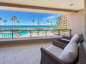 A balcony with wicker furniture, a pool, palm trees, and a view of the ocean. - Relaxing Oceanview Condo Pools Beach (Puerto Peñasco)