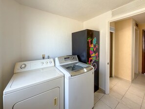 A laundry area with a washer and dryer, a black cabinet with a colorful lizard decal, and a door leading to another room. - Relaxing Oceanview Condo Pools Beach (Puerto Peñasco)