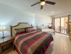 A bedroom with two beds, a ceiling fan, a nightstand with a lamp, and a sliding glass door leading to a balcony. - Relaxing Oceanview Condo Pools Beach (Puerto Peñasco)