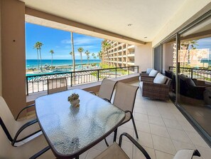 A balcony with a glass table, wicker furniture, and a view of the beach and pool. - Relaxing Oceanview Condo Pools Beach (Puerto Peñasco)