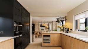 A modern kitchen with black cabinets, a wooden island, and a dining area in the background. - Spacious Countryside Home Yoga Studio (Haverfordwest)