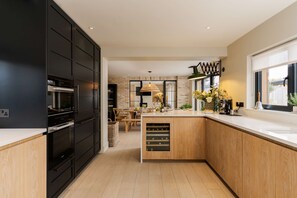 Una cocina moderna con armarios negros, una isla de madera y un comedor al fondo.
