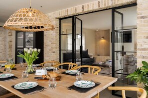 A dining area with a wooden table set for four, a wicker pendant light, and a view into a living space with a black sofa and glass doors. - Spacious Countryside Home Yoga Studio (Haverfordwest)