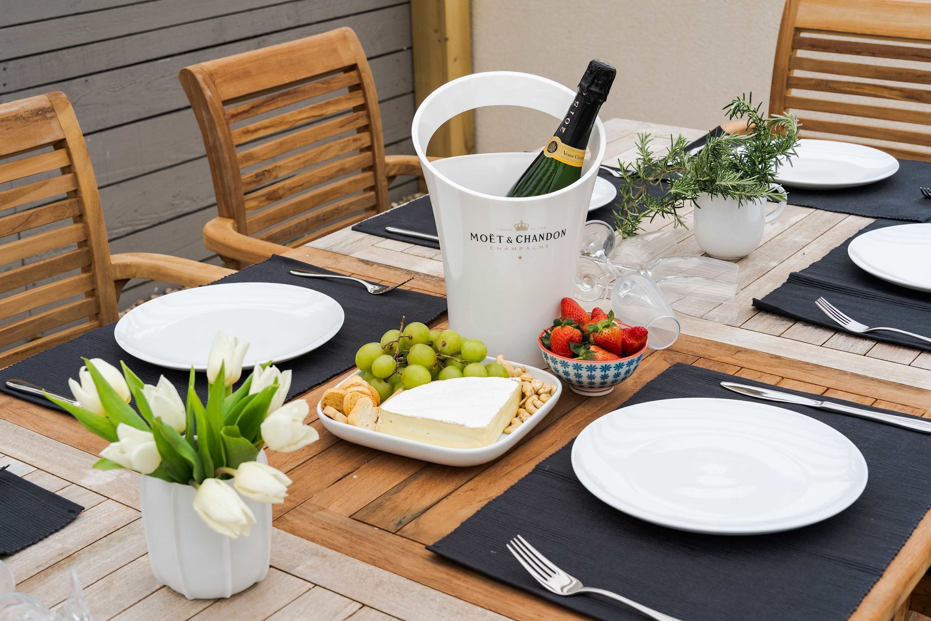 Une table mise pour un repas, avec des assiettes, des couverts, une bouteille de champagne et un vase rempli de fleurs.