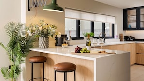 A modern kitchen with a large island, bar stools, a hanging light fixture, and a view through a large window. - Spacious Countryside Home Yoga Studio (Haverfordwest)