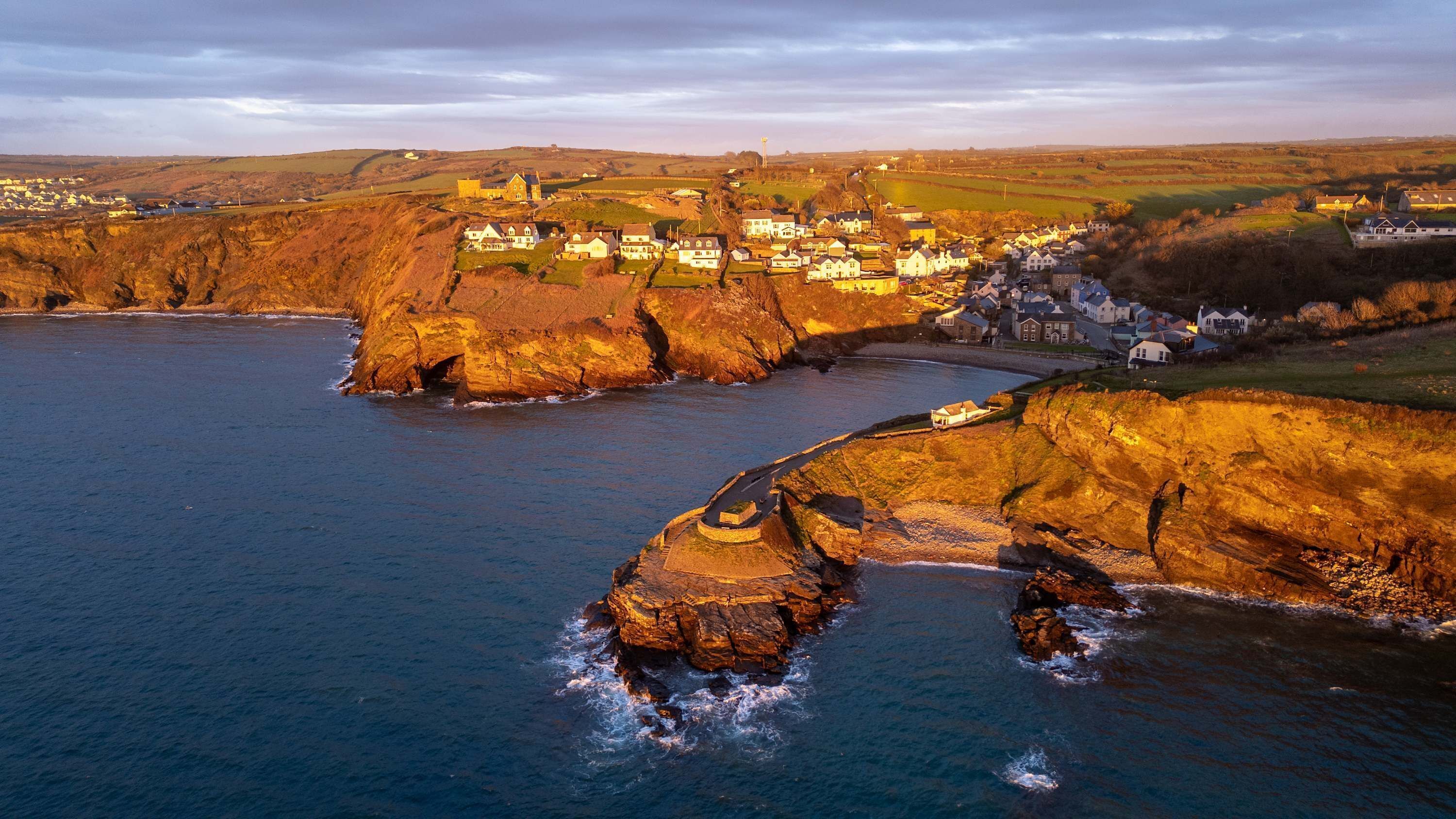 A coastal village with houses along the cliffs, a sea view, and a prominent rock formation.