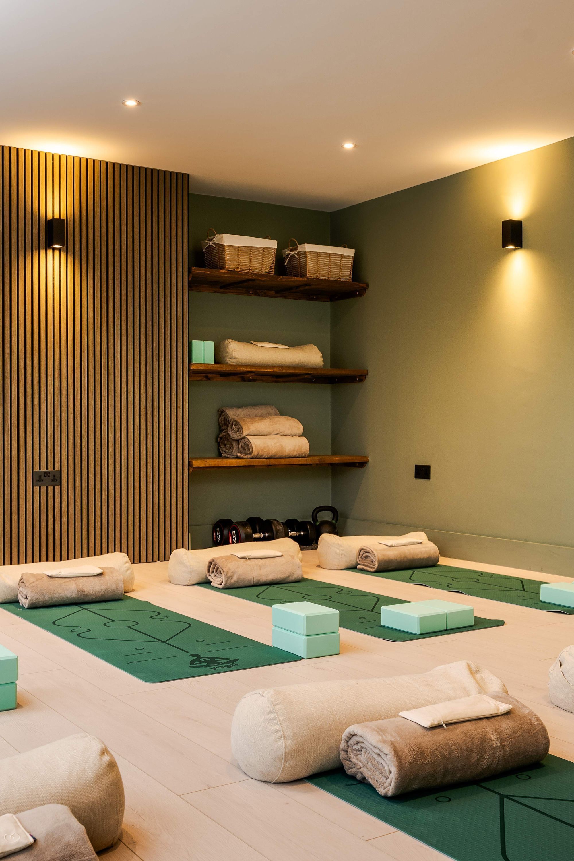 A spa room with wooden paneling, shelves with towels, and a green exercise mat area.