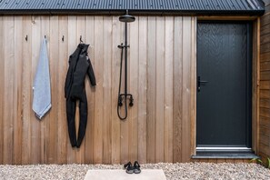 A wooden wall with a black door, a shower, and a pair of shoes on the ground. - Spacious Countryside Home Yoga Studio (Haverfordwest)