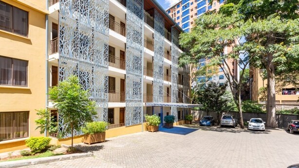 A multi-story building with a courtyard, potted plants, and parked cars. - Tanga Suites (Nairobi)